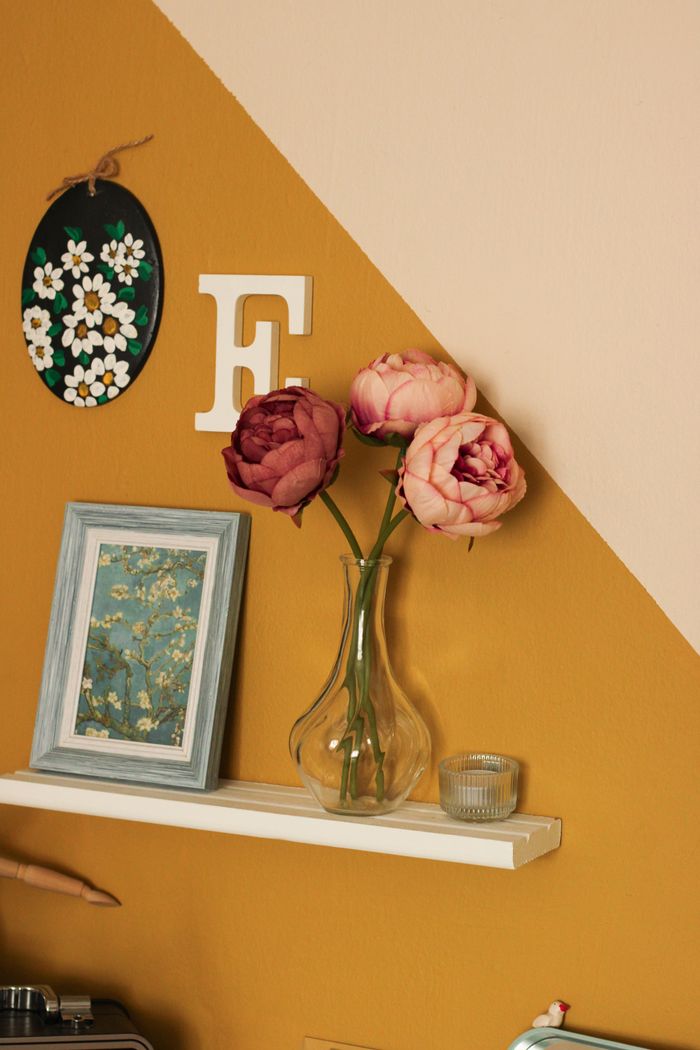 Aesthetic home decor with peonies in glass vase against a vintage yellow backdrop.